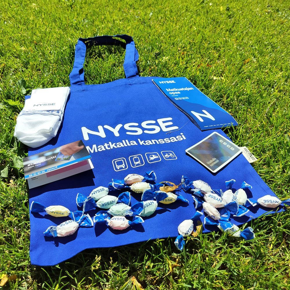 Nysse cloth bag, Nysse socks, gift card case, travel card case and Nysse candy on the lawn.