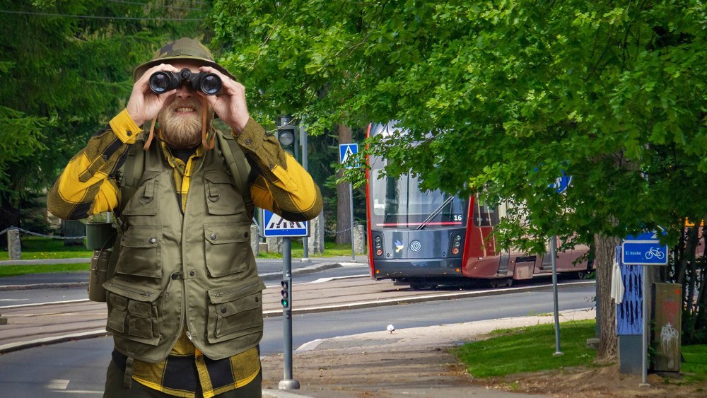 A bearded man dressed in special equipment squints. In the background, a red tram in a summer landscape. 